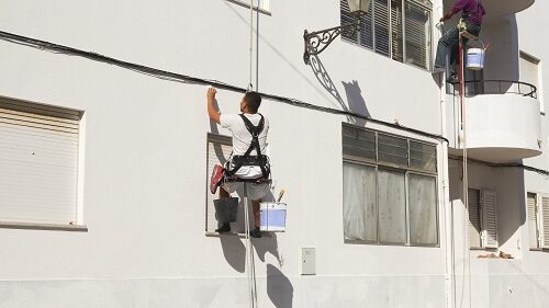 Two painters in harnasses working on a wall in Portugal